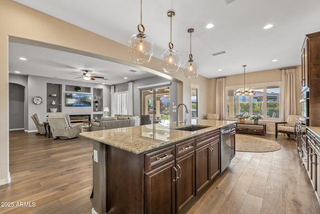 kitchen with built in shelves, light stone countertops, sink, an island with sink, and pendant lighting