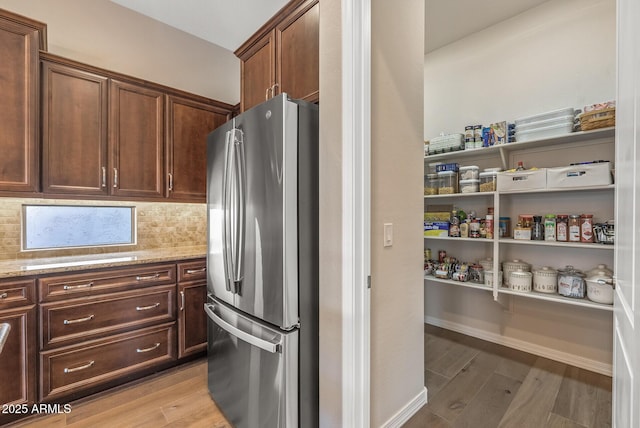 kitchen with light stone countertops, stainless steel fridge, light wood-type flooring, tasteful backsplash, and dark brown cabinetry