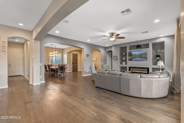 living room with wood-type flooring, ceiling fan with notable chandelier, and built in features