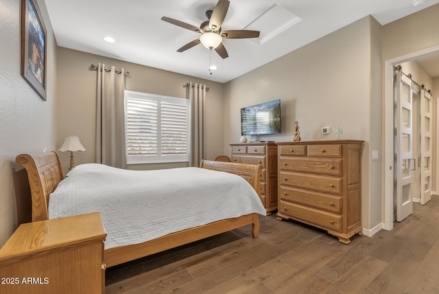 bedroom featuring hardwood / wood-style flooring, ceiling fan, and a barn door