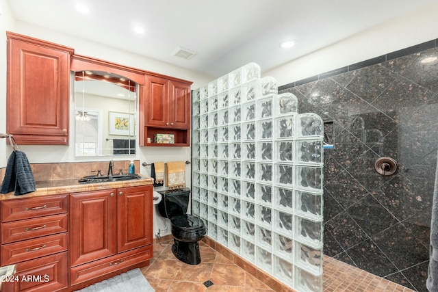 bathroom featuring tile patterned flooring, a tile shower, vanity, and toilet