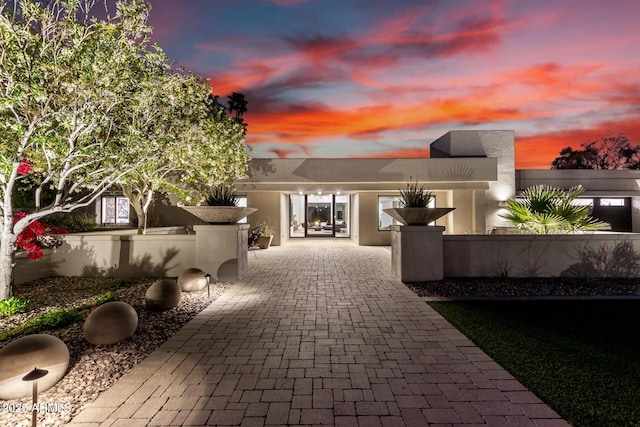 back of house at dusk with a fenced front yard, decorative driveway, and stucco siding