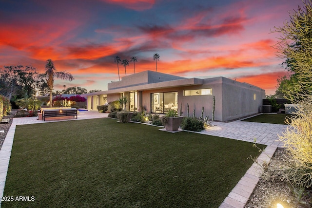 back of property at dusk with a patio, a lawn, stucco siding, and an outdoor living space