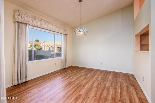 spare room with wood finished floors, baseboards, vaulted ceiling, a textured ceiling, and a notable chandelier