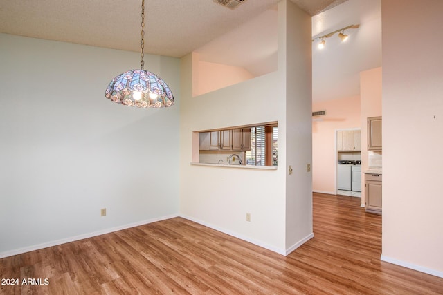 spare room featuring light wood finished floors, baseboards, high vaulted ceiling, and washer and clothes dryer