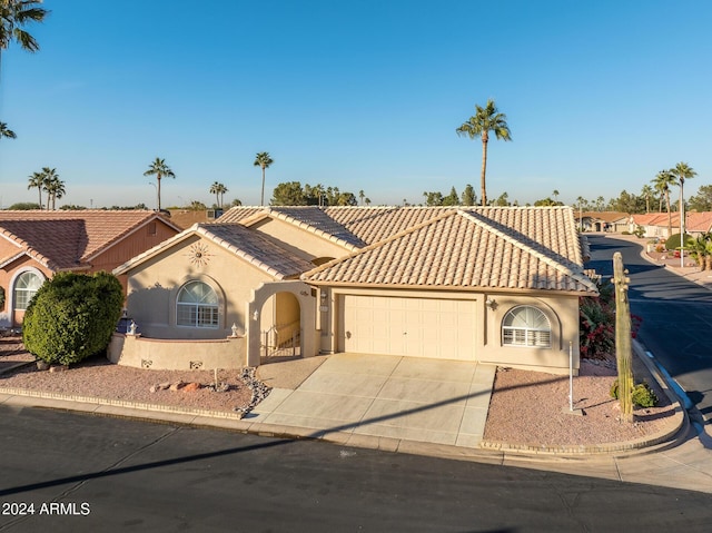 mediterranean / spanish house featuring stucco siding, driveway, an attached garage, and a tile roof