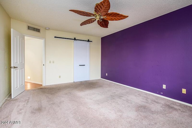 unfurnished bedroom with visible vents, a barn door, a textured ceiling, and carpet floors