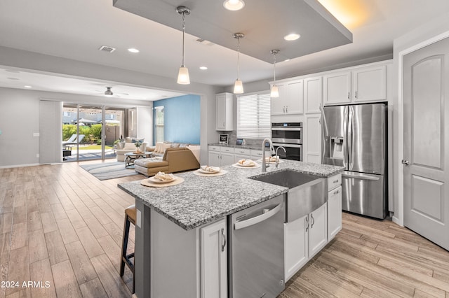 kitchen with a center island with sink, white cabinetry, light stone countertops, light hardwood / wood-style flooring, and stainless steel appliances