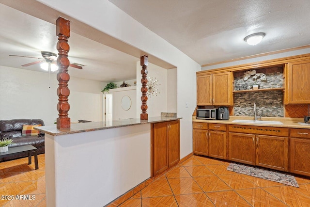 kitchen featuring stainless steel microwave, brown cabinets, a peninsula, a sink, and backsplash