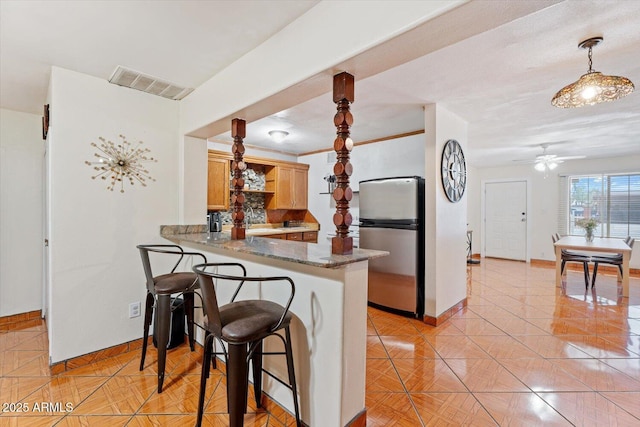 kitchen with visible vents, decorative backsplash, a ceiling fan, freestanding refrigerator, and a peninsula