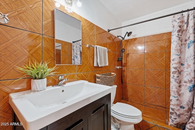 full bathroom with a tile shower, tile walls, toilet, and vanity