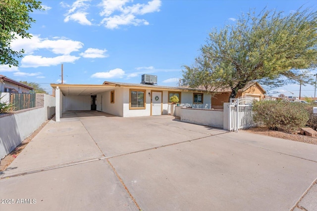 single story home featuring central AC unit, a fenced front yard, driveway, stucco siding, and a carport