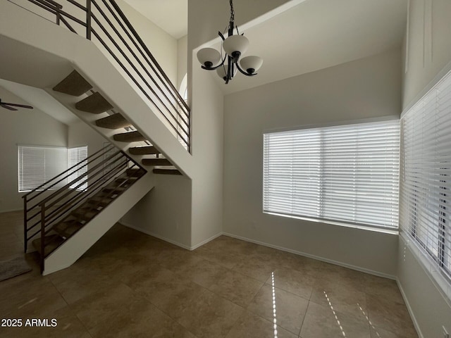 interior space featuring tile patterned floors, stairway, baseboards, and ceiling fan with notable chandelier