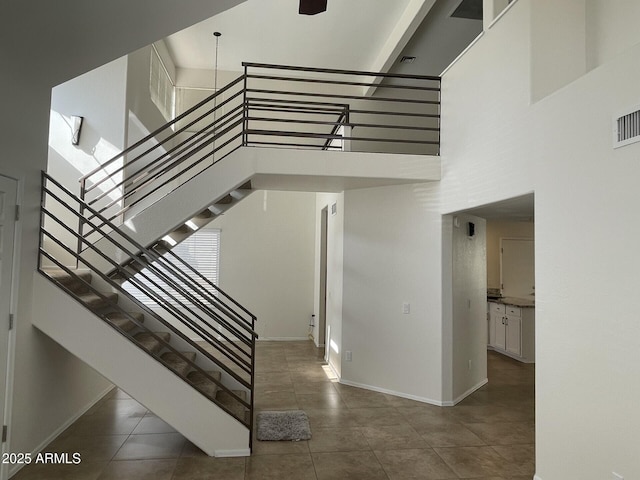 staircase featuring tile patterned floors, a high ceiling, visible vents, and baseboards