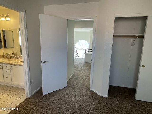 unfurnished bedroom featuring light tile patterned flooring, a sink, a closet, ensuite bathroom, and light colored carpet