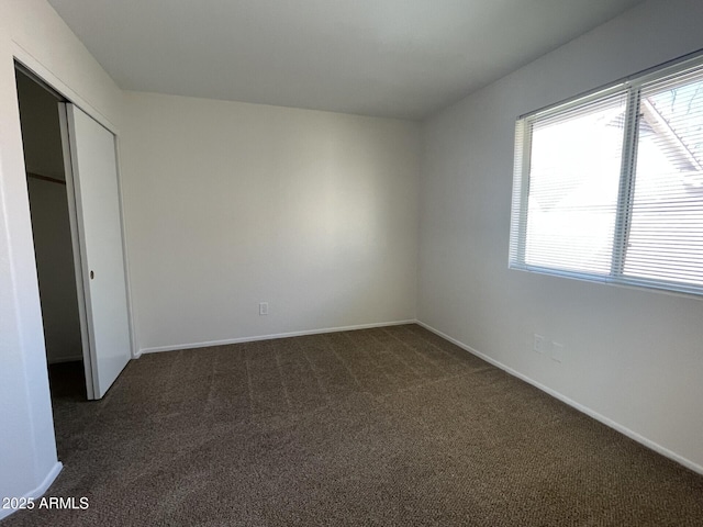 unfurnished bedroom featuring baseboards, dark colored carpet, and a closet