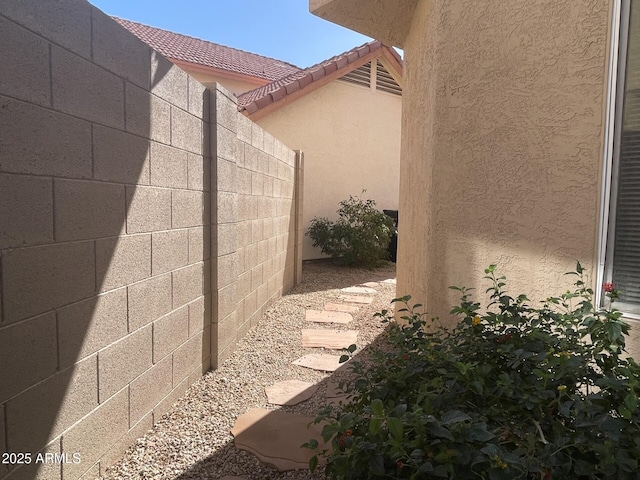 view of side of home with a tile roof, fence, and stucco siding