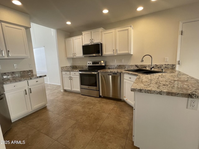 kitchen featuring recessed lighting, appliances with stainless steel finishes, a peninsula, white cabinets, and a sink