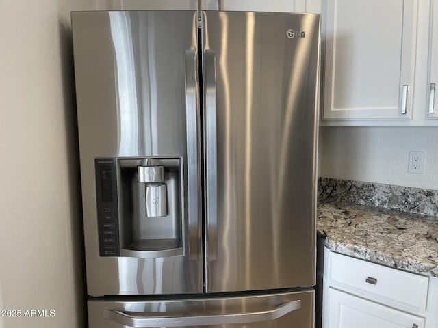 room details featuring light stone countertops, stainless steel fridge with ice dispenser, and white cabinetry