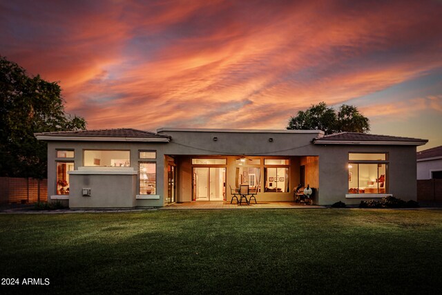 back house at dusk with a patio area and a yard