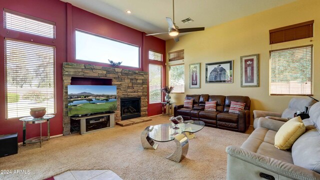 living room with ceiling fan, a towering ceiling, light carpet, and a stone fireplace