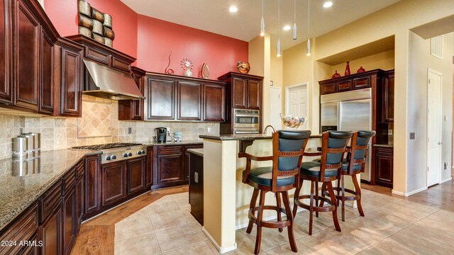 kitchen with stainless steel appliances, ventilation hood, dark stone counters, and a kitchen island