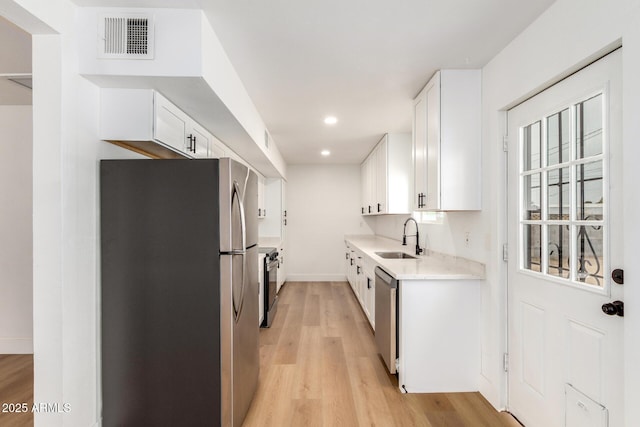 kitchen featuring visible vents, stainless steel appliances, light wood-style floors, white cabinetry, and a sink