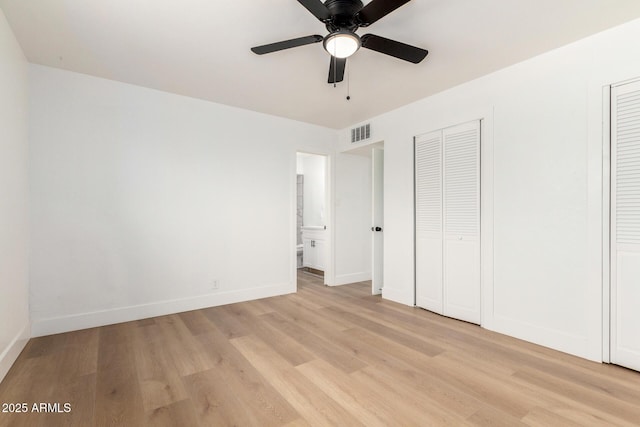 unfurnished bedroom with baseboards, visible vents, ensuite bath, light wood-type flooring, and multiple closets