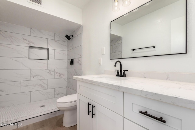 bathroom featuring toilet, tiled shower, wood finished floors, and vanity