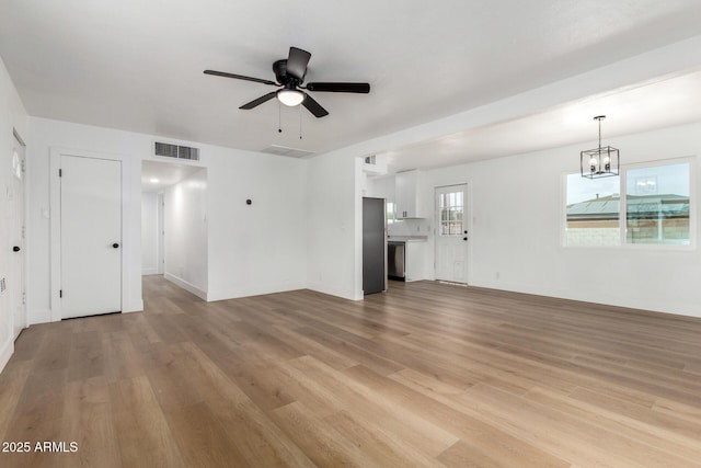 unfurnished living room featuring light wood-type flooring, baseboards, visible vents, and ceiling fan with notable chandelier