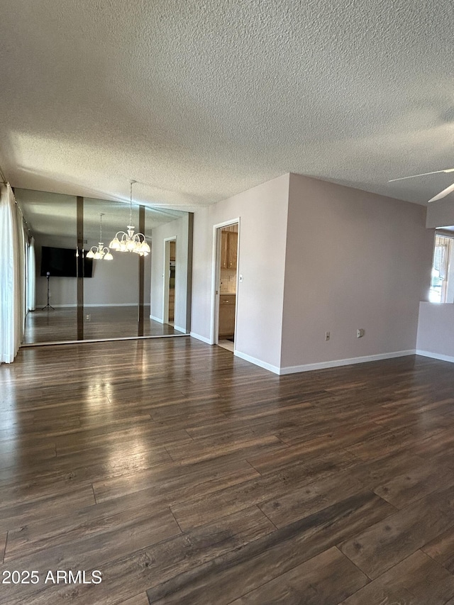 empty room with dark wood-type flooring, a textured ceiling, and a chandelier