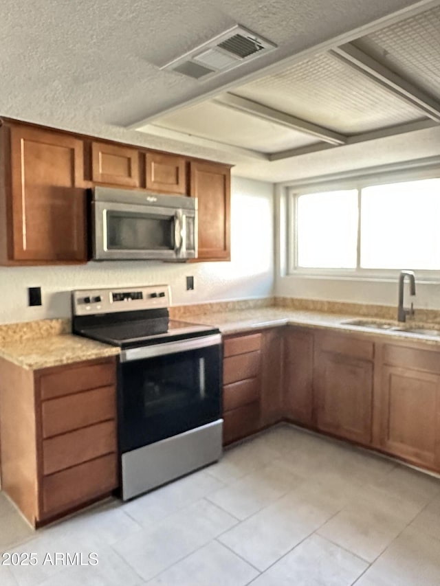 5924 W Tierra Buena Ln, Glendale, AZ 85306 - kitchen with stainless steel appliances, a sink, brown cabinetry, a textured ceiling, and light tile patterned floors