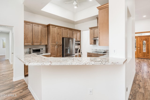 kitchen with light hardwood / wood-style floors, kitchen peninsula, light stone counters, and stainless steel fridge with ice dispenser