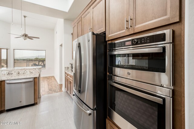 kitchen featuring ceiling fan, appliances with stainless steel finishes, light stone counters, and light hardwood / wood-style flooring