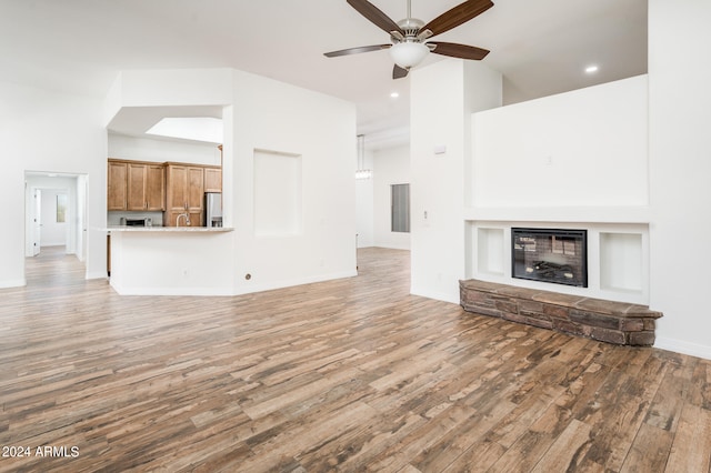 unfurnished living room with ceiling fan, a fireplace, hardwood / wood-style floors, and a high ceiling