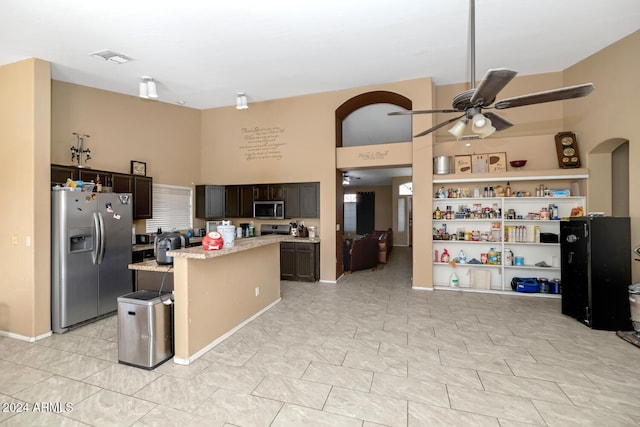 kitchen with dark brown cabinetry, light stone counters, appliances with stainless steel finishes, a towering ceiling, and a kitchen island