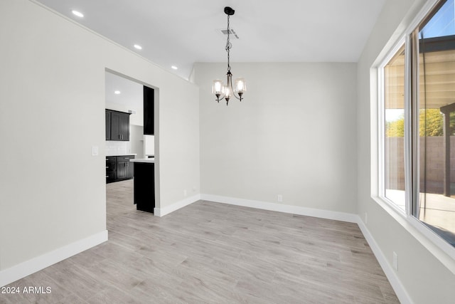 spare room with a chandelier, lofted ceiling, and light hardwood / wood-style flooring