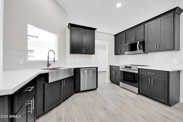 kitchen with tasteful backsplash, sink, appliances with stainless steel finishes, and light hardwood / wood-style flooring