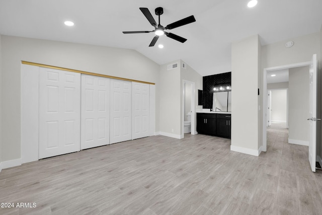 unfurnished bedroom with vaulted ceiling, ensuite bath, ceiling fan, light wood-type flooring, and a closet