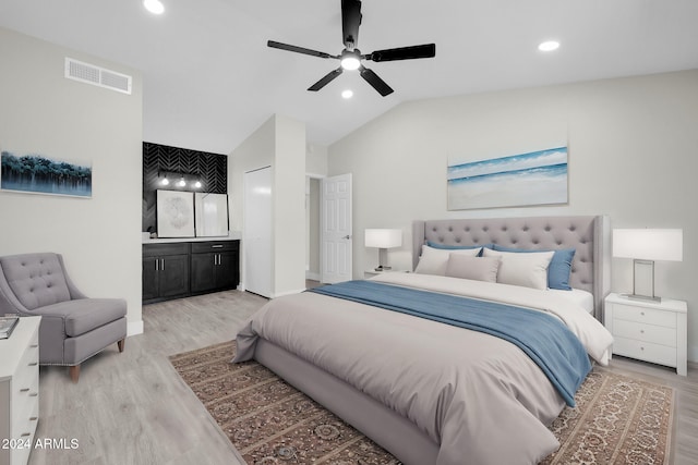 bedroom featuring light wood-type flooring, ensuite bathroom, vaulted ceiling, and ceiling fan