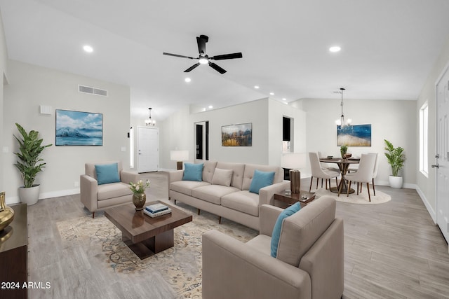 living room with ceiling fan with notable chandelier, light hardwood / wood-style floors, and vaulted ceiling