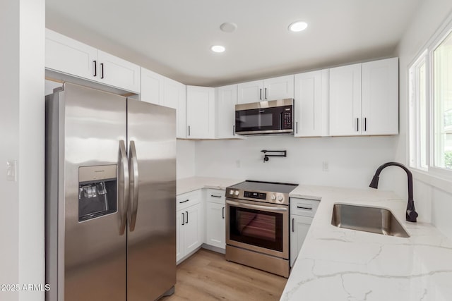 kitchen featuring light stone countertops, light wood-type flooring, white cabinets, a sink, and appliances with stainless steel finishes