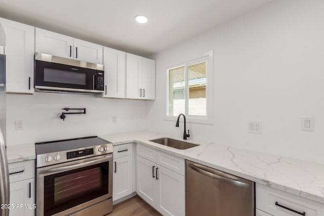 kitchen with light stone countertops, recessed lighting, white cabinets, a sink, and stainless steel appliances