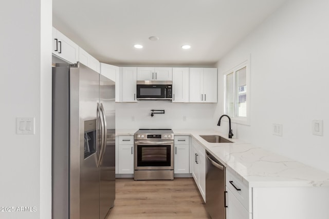 kitchen with appliances with stainless steel finishes, light stone countertops, light wood-type flooring, a sink, and white cabinetry