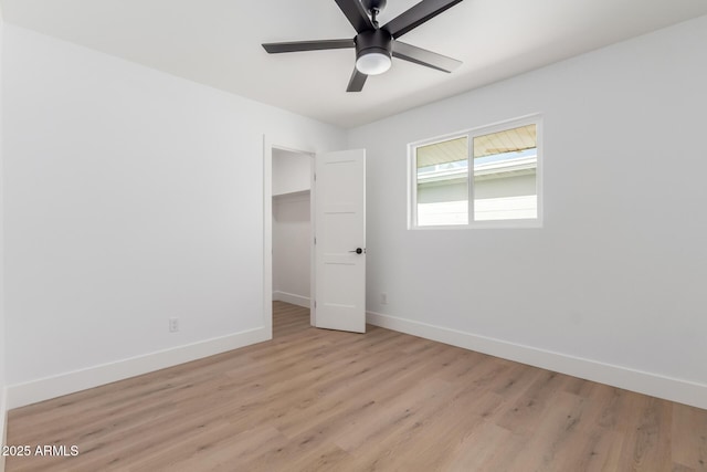 unfurnished bedroom with a closet, baseboards, a spacious closet, and light wood-style floors