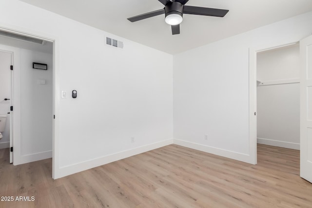 unfurnished bedroom with baseboards, visible vents, a walk in closet, and light wood-style floors