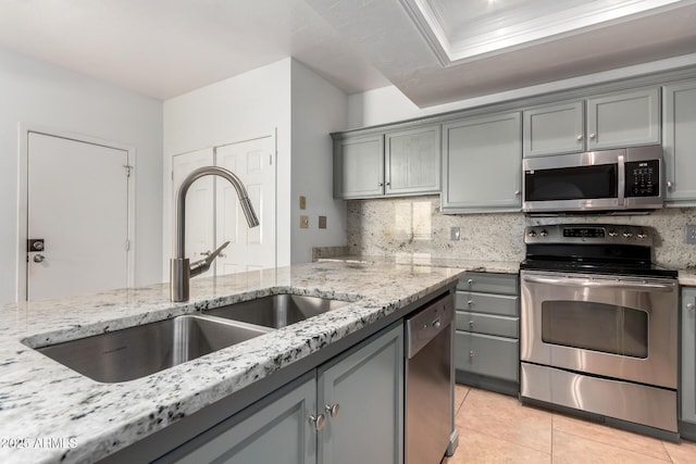 kitchen featuring sink, gray cabinetry, appliances with stainless steel finishes, light stone countertops, and backsplash