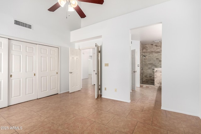 unfurnished bedroom with ensuite bathroom, light tile patterned floors, a closet, ceiling fan, and a high ceiling