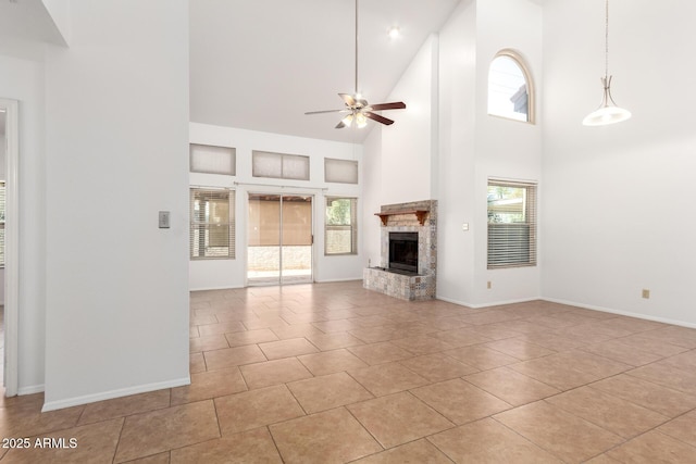 unfurnished living room featuring light tile patterned flooring, ceiling fan, a stone fireplace, and a towering ceiling