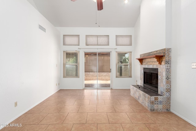 unfurnished living room featuring light tile patterned floors, a towering ceiling, a tile fireplace, and ceiling fan